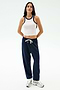 A person stands against a plain background wearing the SPLITS59 Kiki Rib Crop Tank in White/Indigo, navy blue drawstring sweatpants, and white sneakers.