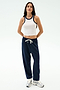 A person stands against a plain background wearing the SPLITS59 Kiki Rib Crop Tank in White/Indigo, navy blue drawstring sweatpants, and white sneakers.