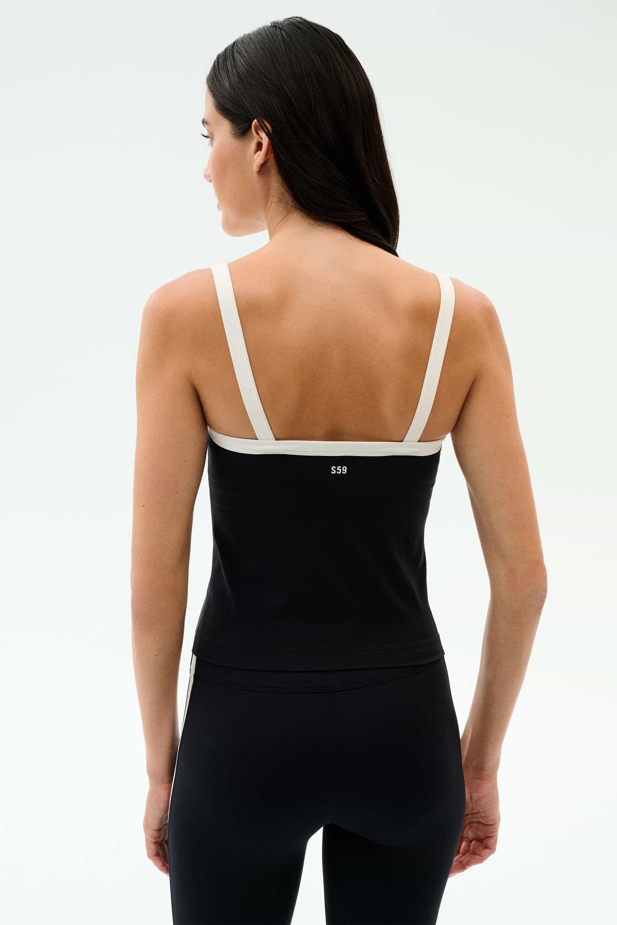 A woman wears the SPLITS59 Monah Rigor Tank in Black/White with black leggings, standing against a white background—an ideal look for gym workouts.
