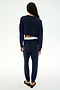 Wearing the SPLITS59 Andie Dual Waist Sweatpant in Indigo/White, this person—proudly made in Los Angeles—stands with their back to the camera, styled with a navy blue long-sleeve top, black flats, and a visible white waistband crafted from ultra-luxe fleece.