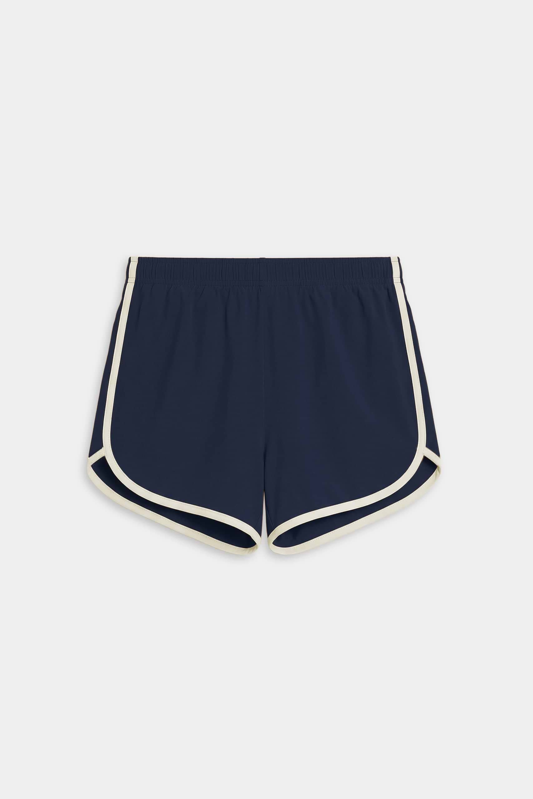 The SPLITS59 Megan Woven Nylon Run Short in Indigo/Creme features a curved hem, elastic waistband, and white trim. Made from a comfortable spandex-nylon blend, the shorts are displayed flat on a white background.