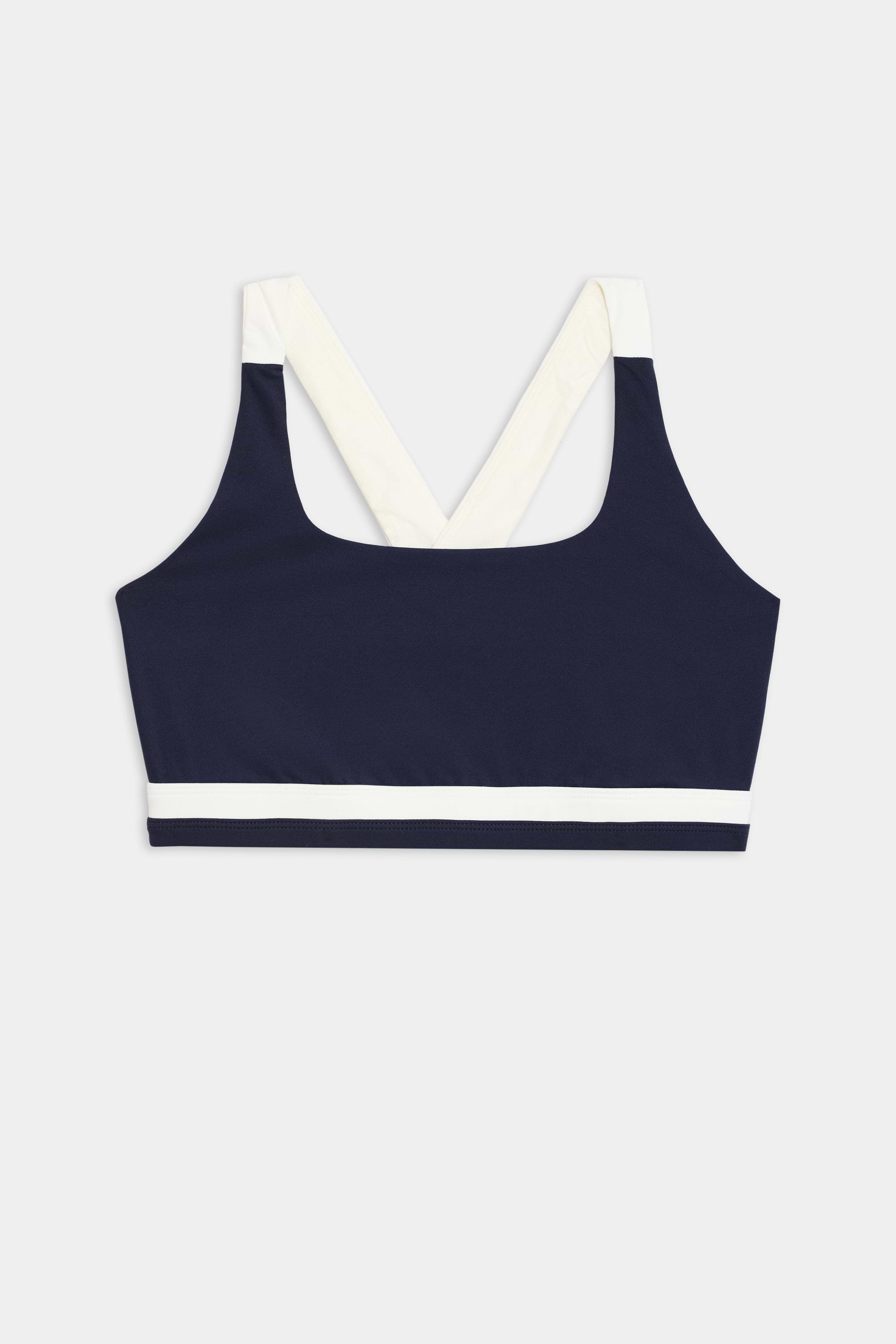 The Miles Rigor Bra by SPLITS59, featuring a navy design with wide white straps and a white band under the bust, is displayed on a light gray background.