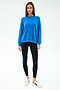 A woman faces forward against a plain light background, wearing the SPLITS59 Andie Oversize Fleece Sweatshirt in Classic Blue and black leggings with a blue stripe, paired with white sneakers.