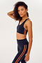 Side view of girl wearing dark blue sports bra with two thin red stripes down the side and dark blue leggings