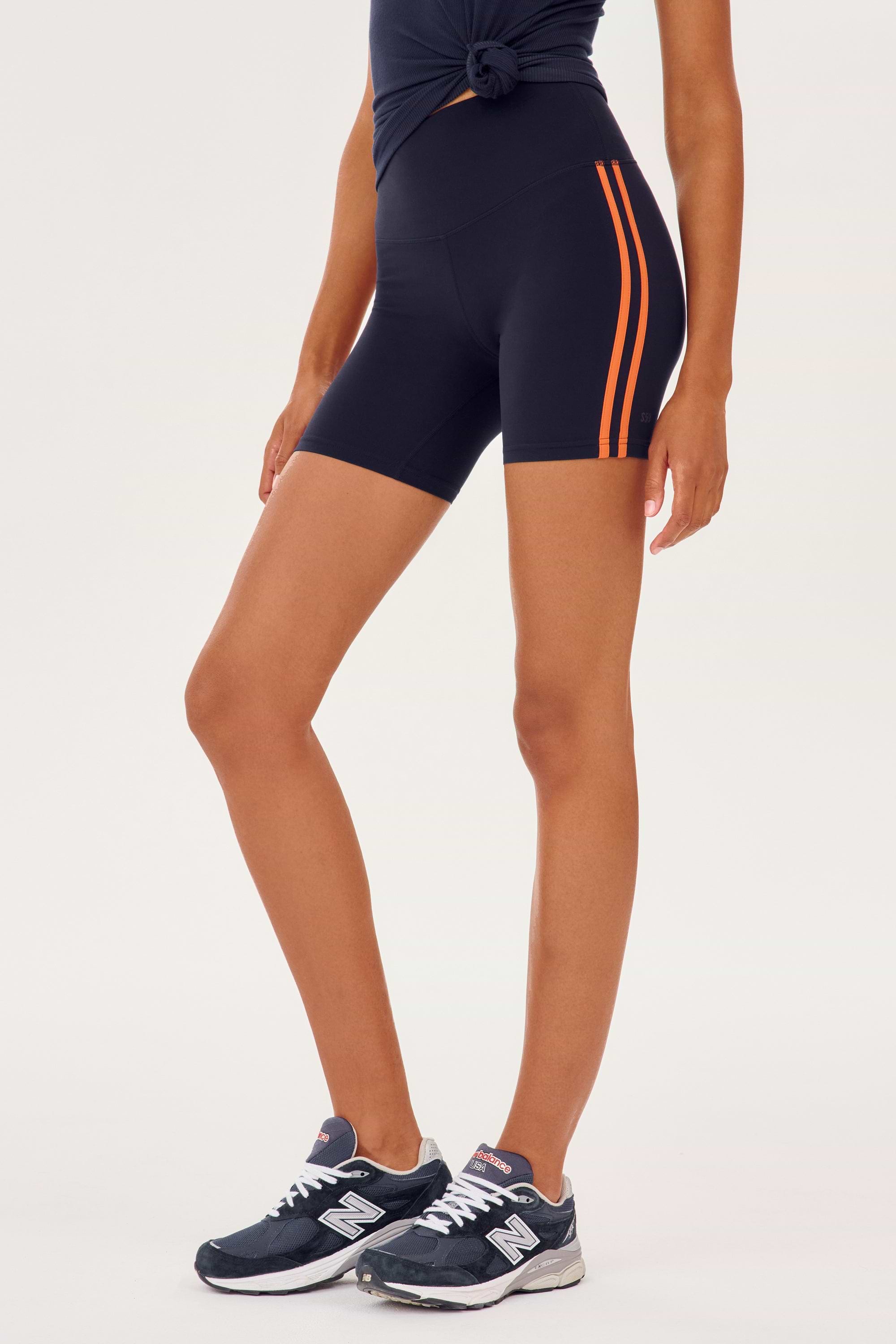 Side view of girl wearing dark blue bike sorts with two thin red stripes down the side that stop upper thigh with dark blue shoes