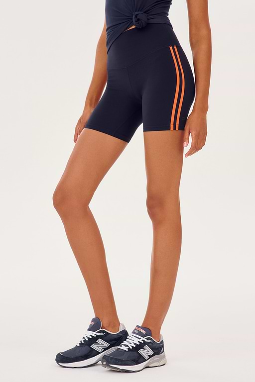 Side view of girl wearing dark blue bike sorts with two thin red stripes down the side that stop upper thigh with dark blue shoes