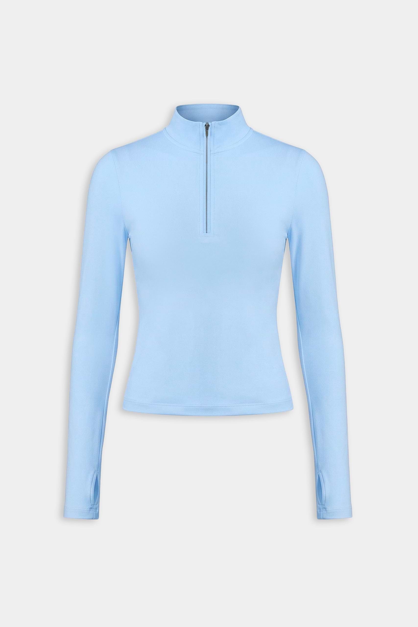The SPLITS59 Tess Rigor Half Zip Waist Length in Skylight is a women's light blue long-sleeve top with a mock neck and front half-zip, made from a soft nylon-spandex blend, shown against a plain white background.