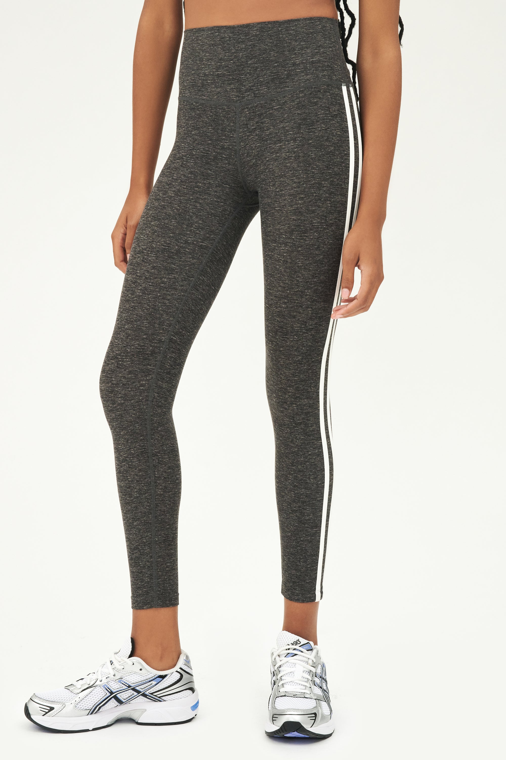 Front view of girl wearing dark grey leggings with thin white and black stripes down the side with white shoes
