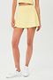 Front view of girl wearing light yellow upper thigh skirt with built in shorts and white shoes