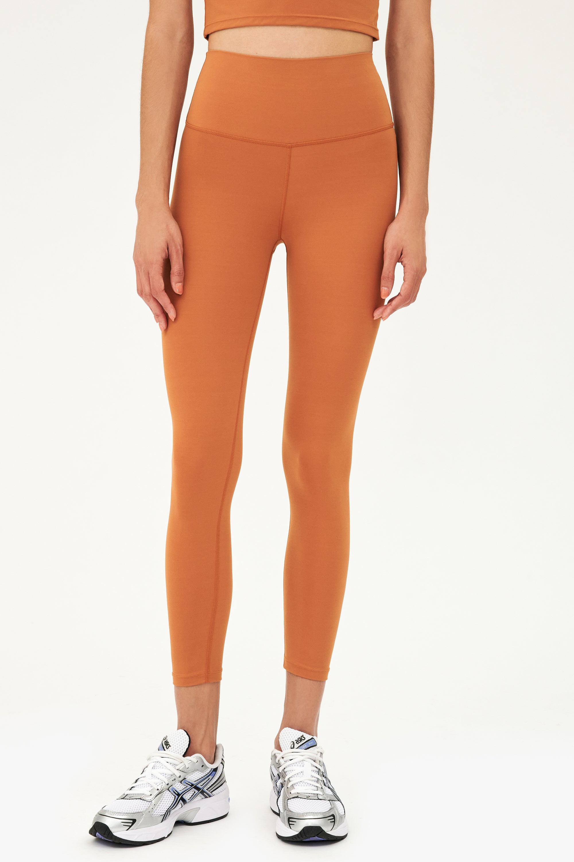 Front view of model wearing a dark orange bra tank with dark orange high waist leggings and white shoes with black stripes