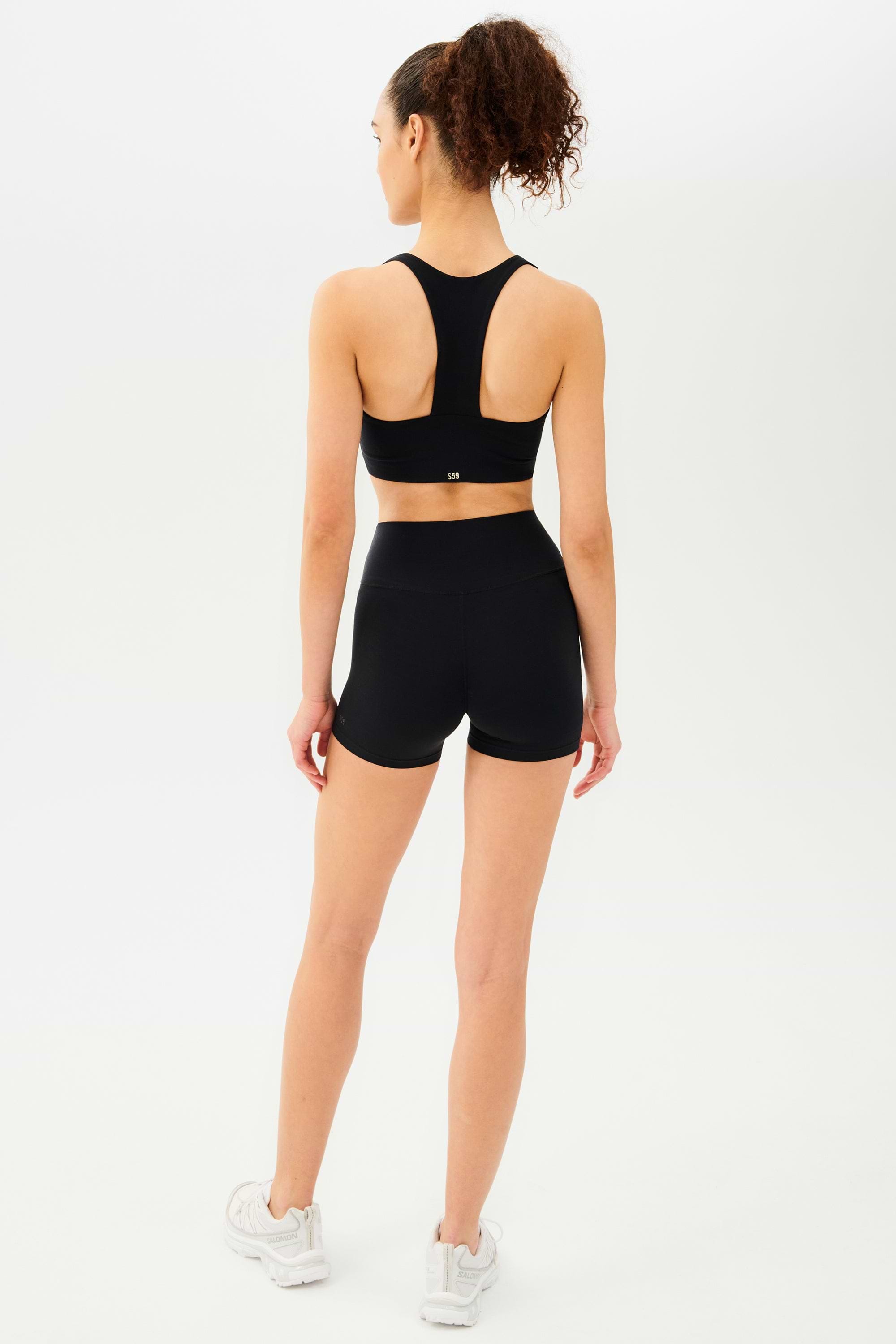 Full back view of girl wearing black shorts with black sports bra and white shoes