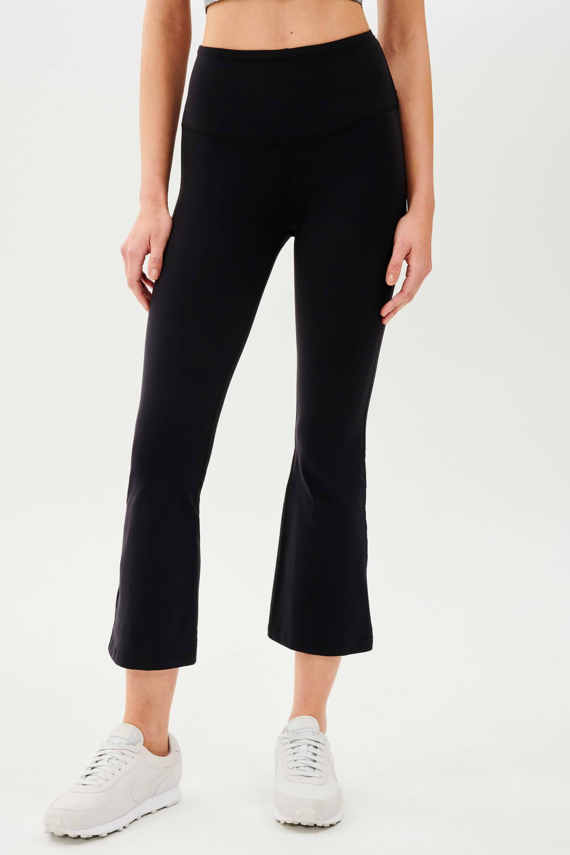 A woman wearing SPLITS59's Raquel High Waist Crop leggings in black and a white tee.