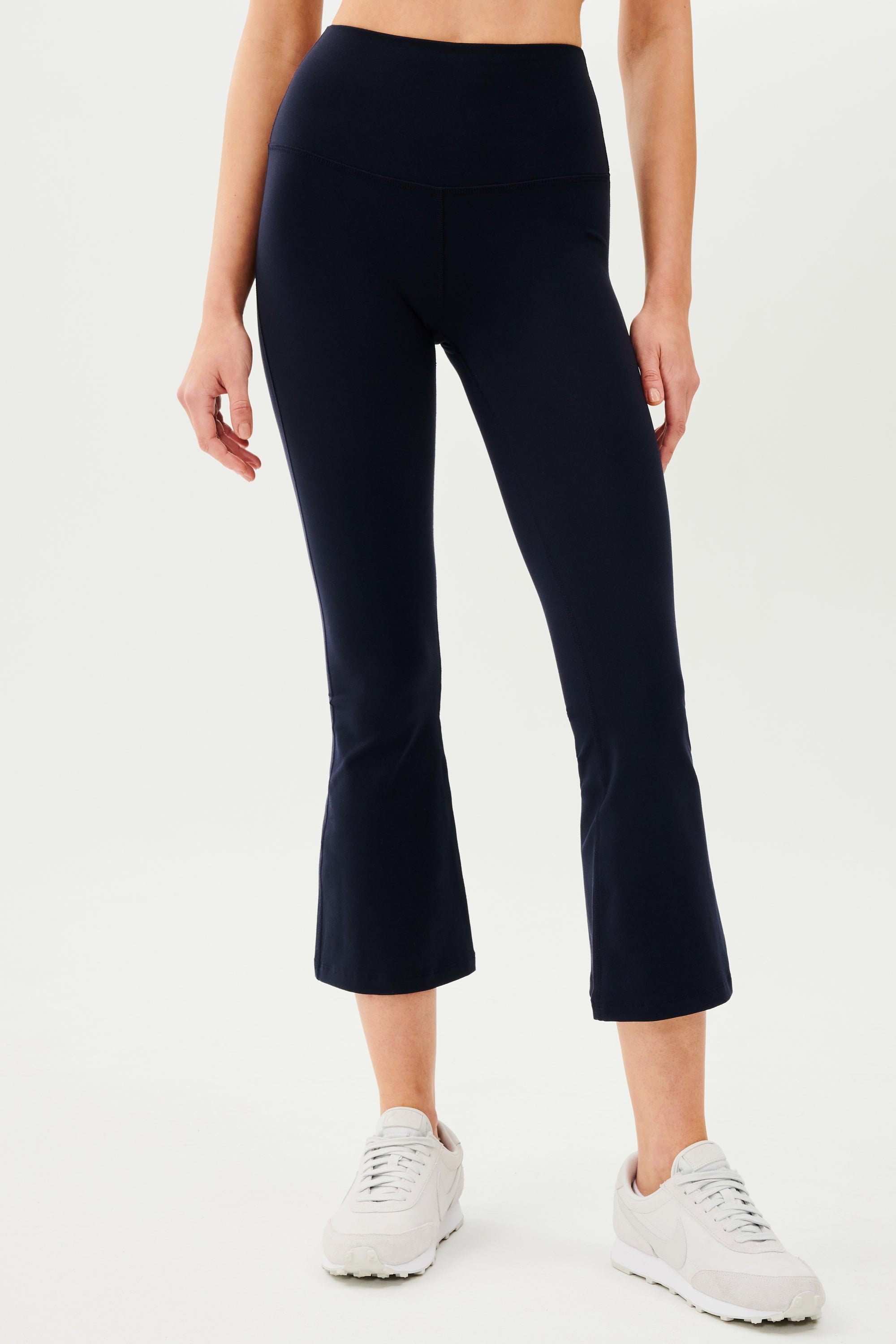 A woman wearing black SPLITS59 Raquel High Waist Crop leggings and white sneakers.