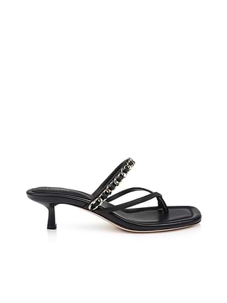 The Georgette Kitten-Heel Sandal features a black leather upper with thin straps, a low kitten heel, and gold chain hardware across the front, displayed against a white background.