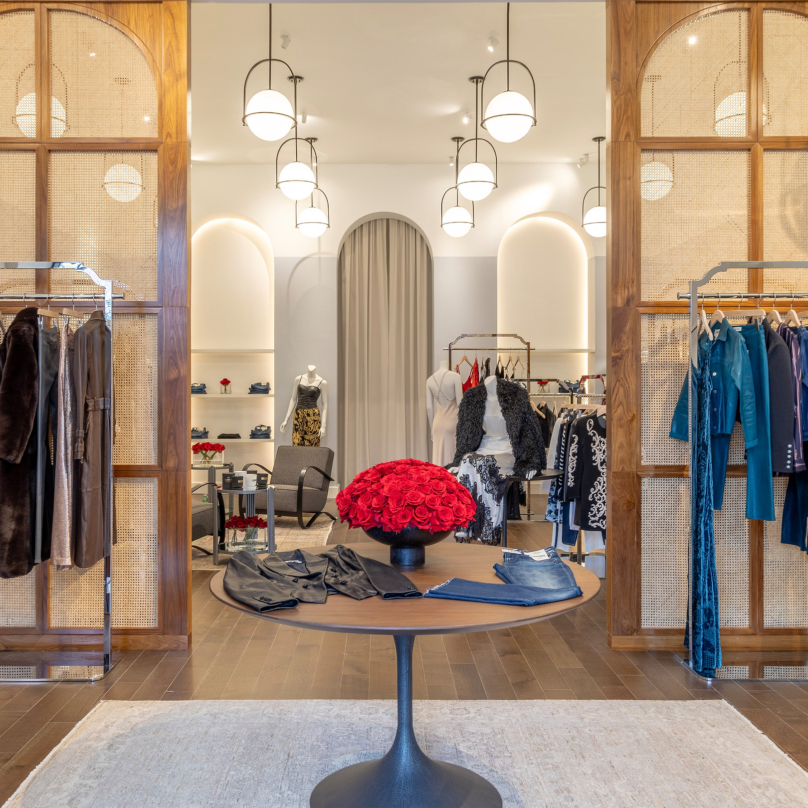 Interno di un elegante negozio di abbigliamento con espositori, un tavolo con una composizione floreale rossa e manichini.