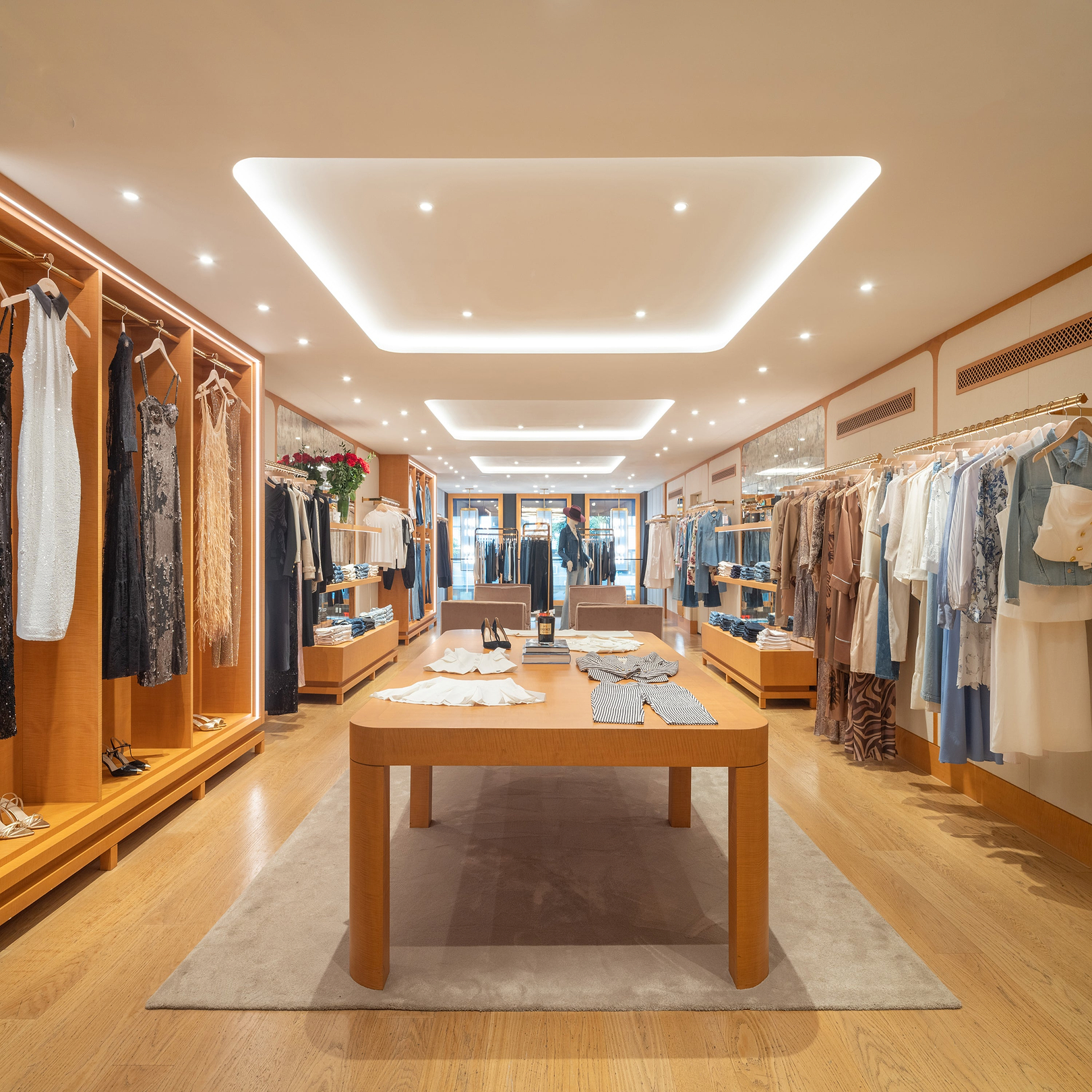Boutique di abbigliamento moderno con pavimenti e scaffali in legno, che espone abiti, camicette e scarpe disposti con cura. Una luce soffusa valorizza i capi, mentre un tavolo centrale presenta abiti piegati e accessori.