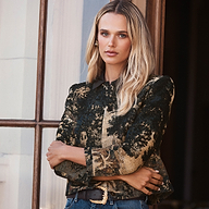 A woman wears a Lian Tapestry Jacket, a structured garment made of dark, Flemish tapestry-style fabric featuring intricate floral patterns.