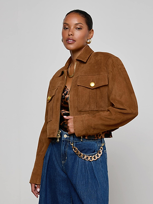 A woman poses in the Micah Oversized Suede Jacket, featuring an oversized fit and gold buttons, styled with a leopard print top, blue jeans, gold hoop earrings, a necklace, and a gold chain belt against a plain light background.