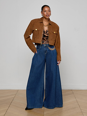 A woman poses indoors in the Micah Oversized Suede Jacket, a leopard print top, wide-leg high-waisted blue jeans with a chain belt, and hoop earrings, standing on a light wood floor against a plain white wall.