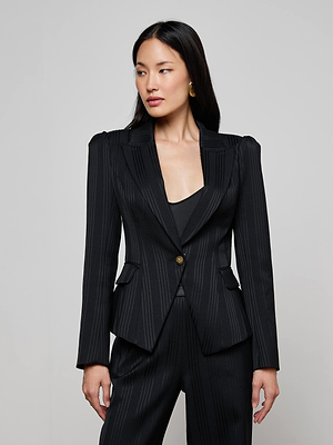 A woman with long dark hair wears the L'AGENCE Kaisley Faux Fur Collar Blazer, styled with matching pants. She stands against a plain light grey background, looking to her left with a neutral expression.