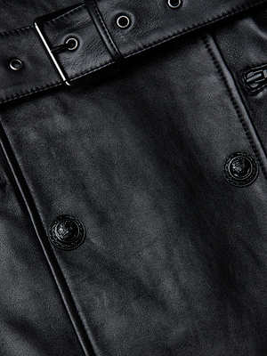Close-up of the Celina Fringed Leather Trench in black lambskin, showcasing a belted waist with a silver buckle, metal grommets, two buttons, and detailed visible stitching.