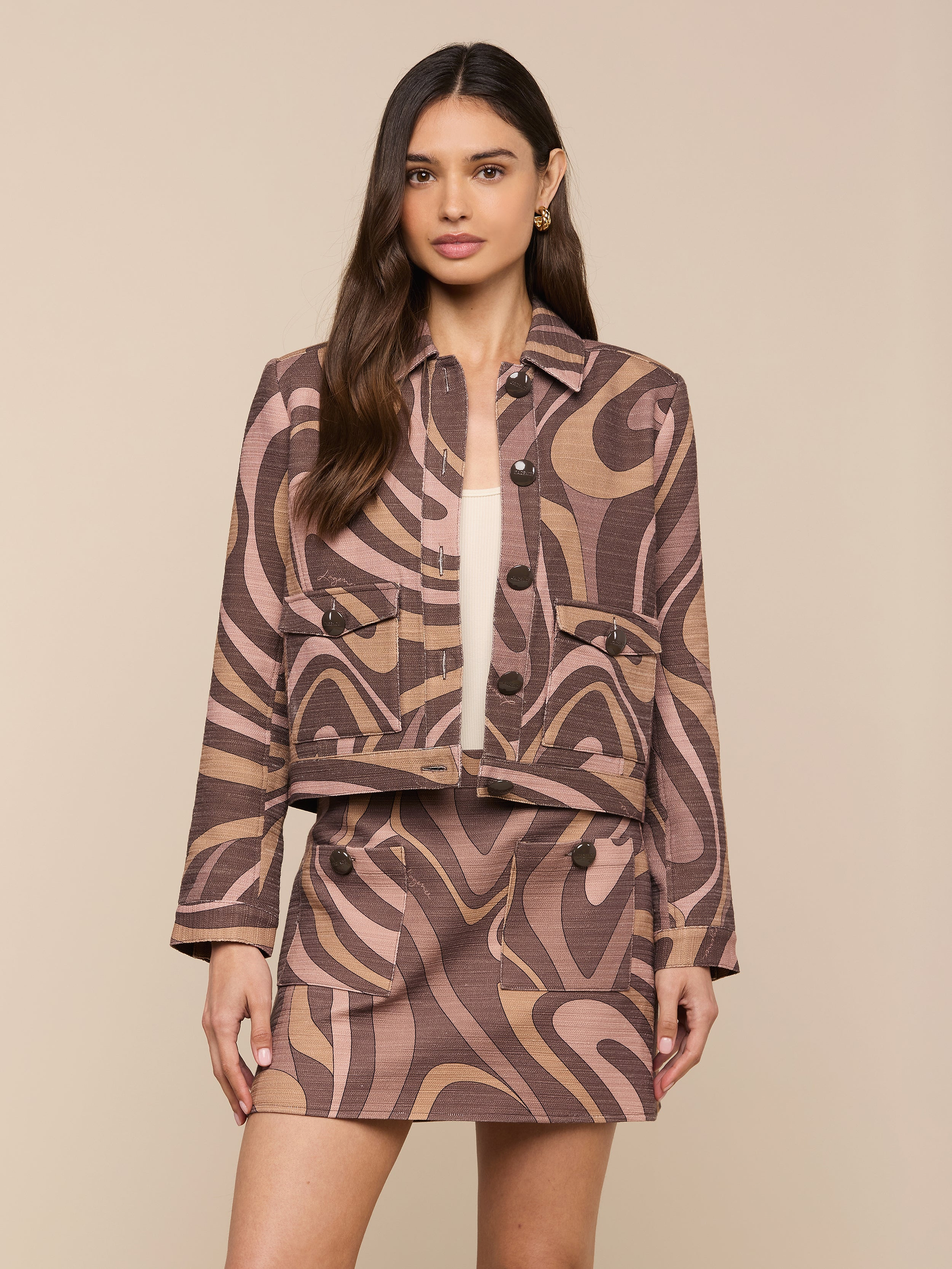 A woman stands facing forward against a plain light background, wearing the Nyx Cropped Jacket, a relaxed fit jacket featuring a brown and beige abstract swirl pattern.