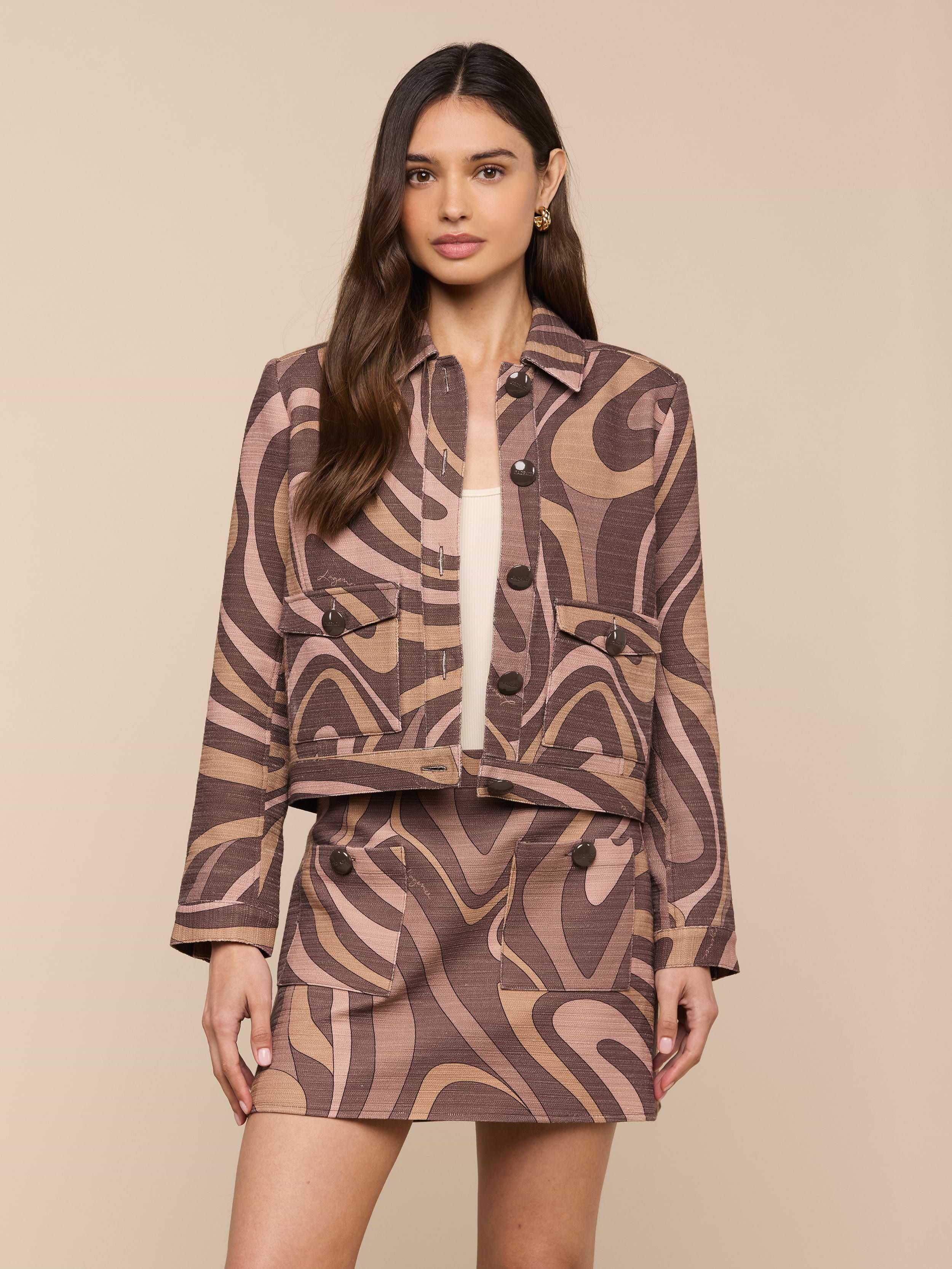 A woman stands facing forward against a plain light background, wearing the Nyx Cropped Jacket, a relaxed fit jacket featuring a brown and beige abstract swirl pattern.
