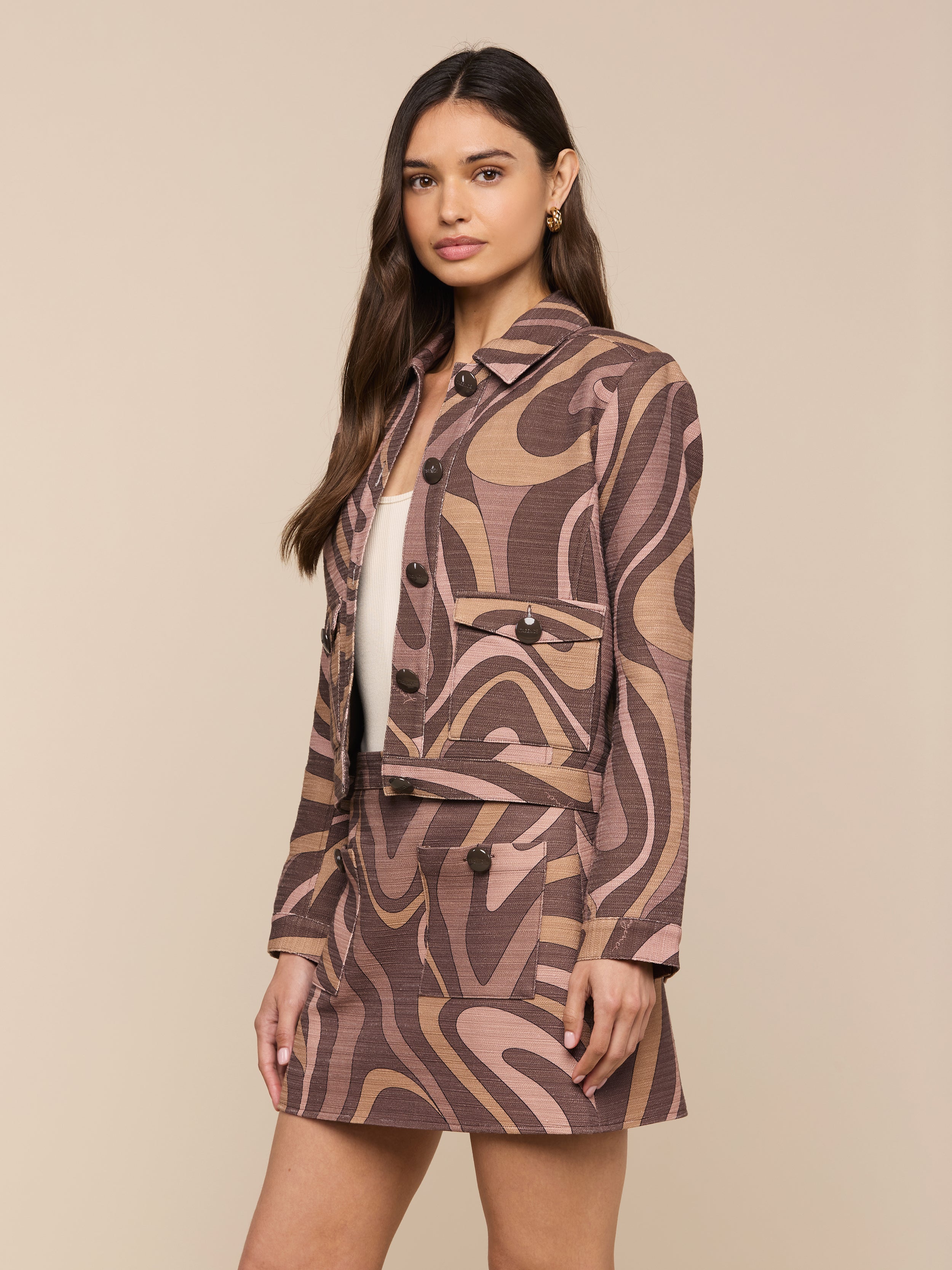 Woman wearing the Nyx Cropped Jacket, a relaxed fit, lightweight cotton jacket with a brown, pink, and beige abstract swirl pattern, paired with a matching skirt and standing against a plain light background.