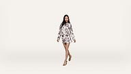 A woman walks confidently, wearing a matching floral-patterned jacket and skirt with a bow at the neck and tan heeled sandals, against a plain white background.