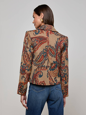 A woman with long brown hair and gold earrings stands with her back to the camera, wearing L'AGENCE's Kelsey Peacoat—a cropped wool-blend jacket with a colorful paisley pattern—paired with classic blue jeans.