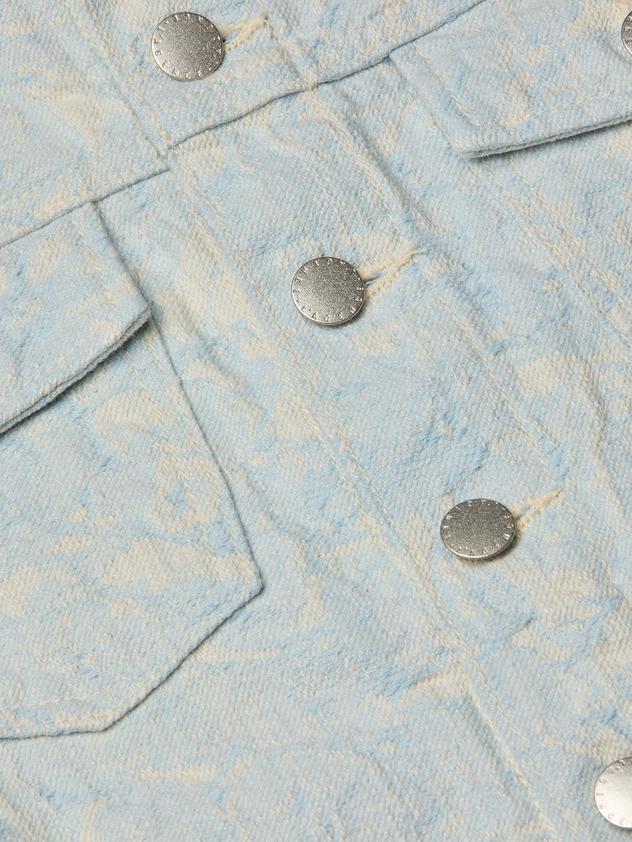 Close-up of the Maven Jacket in light blue textured cotton jacquard, showcasing a subtle floral pattern, two silver metal buttons, and part of a flap pocket for a structured look.