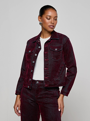 A woman wears the L'AGENCE Maven Flocked Jean Jacket in burgundy with matching pants over a white top, standing against a plain light gray background and looking to the side.