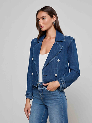 A woman with long brown hair, silver hoop earrings, a white top, blue jeans, and the Maddox Jean Trench Coat stands against a plain light gray background.