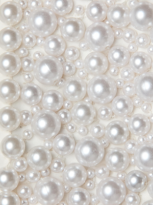 The Belle Oversized Pearl Jacket by L'AGENCE features hand-sewn faux pearls of varying sizes, scattered and clustered together on a light background for a textured, elegant look—a true statement piece.