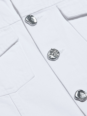 Close-up of the Anouk Jean Jacket in white, made from all-cotton denim. Features two pockets, three shiny, irregular silver buttons, and visible fabric texture with detailed stitching.