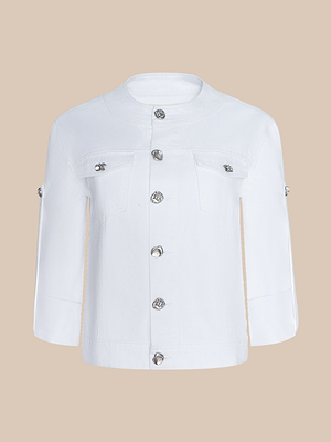 The Anouk Jean Jacket is a white, collarless, all-cotton denim jacket with silver decorative buttons down the front and chest pockets, shown against a beige background.