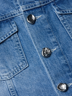 Close-up of the Anouk Jean Jackets indigo denim fabric with silver metallic buttons and a visible pocket flap, showcasing the garments textured material and detailed stitching.