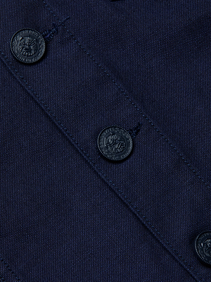 Close-up of the Anouk Jean Jacket in navy blue stretch denim, featuring a diagonal seam and four dark decorative buttons. The collarless design highlights the jacket’s tight weave and texture.
