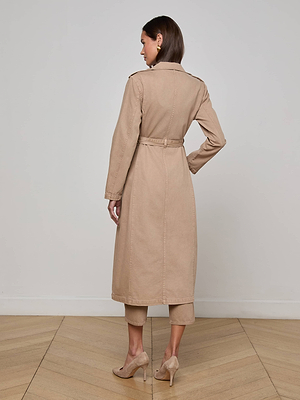 A woman stands indoors facing away, wearing the L’AGENCE Zavia Jean Trench Coat with an oversized collar and waist tie, paired with matching pants and beige heels, on a wooden floor against a plain white wall.