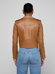A person stands facing away, wearing the Blakely Leather Biker Jacket in brown lambskin and blue jeans. The background is plain and light-colored.