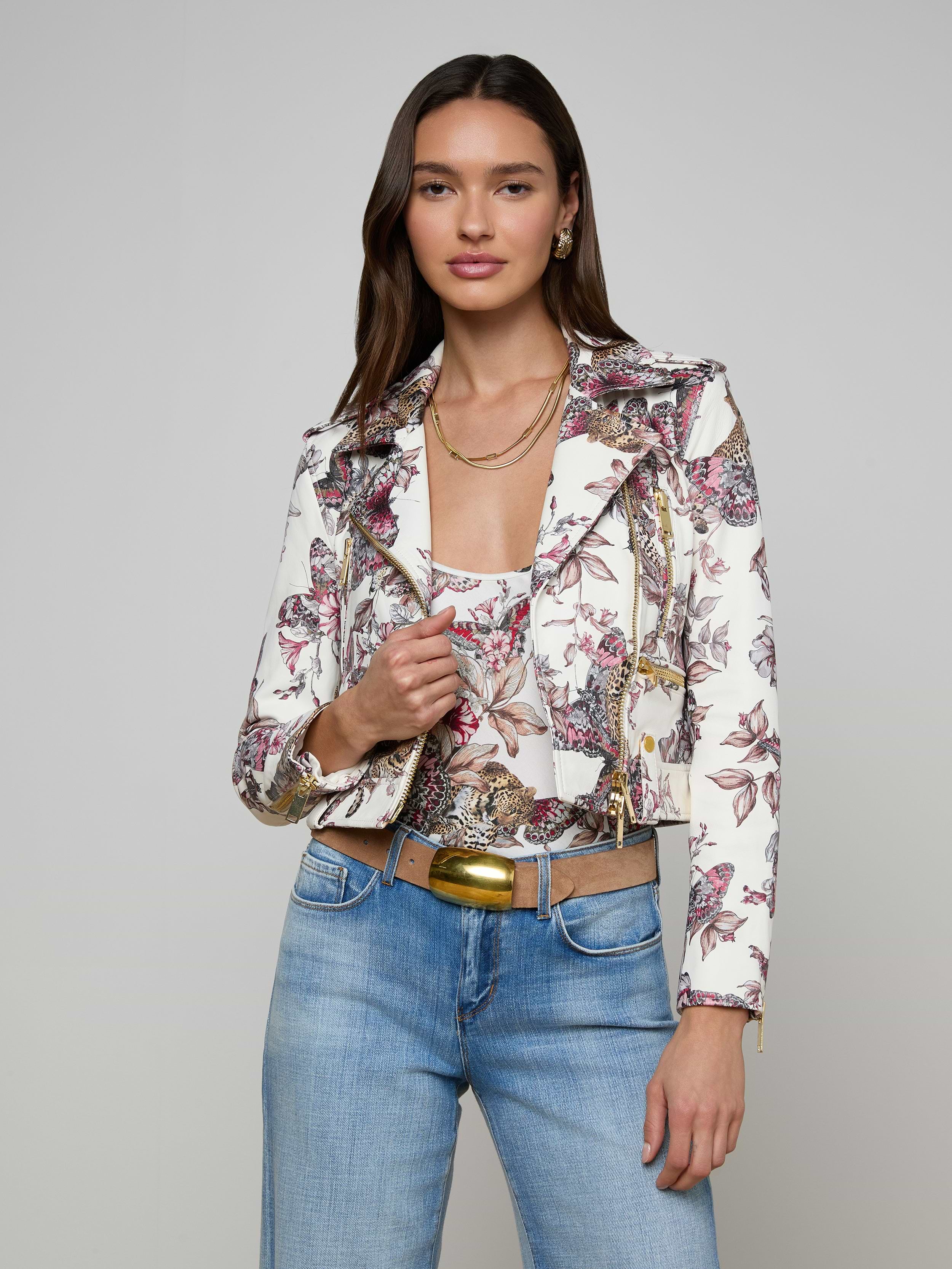 Woman wearing the Blakely Leather Biker Jacket, blue jeans, a gold belt, and layered necklaces, standing against an off-white background.