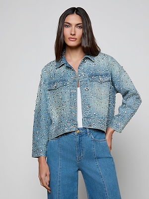 A woman with straight brown hair models the Vangie Embellished Jean Jacket over a white top and blue jeans, standing against a plain light gray background.