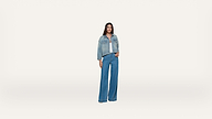 A woman stands against a plain white background, wearing a blue denim jacket over a white top and wide-leg blue jeans. She is facing forward with her arms relaxed by her sides.