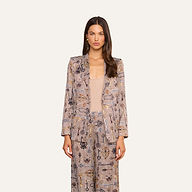 A woman with long brown hair stands against a plain off-white background, facing forward with a neutral expression and her arms relaxed at her sides. She wears the Aven Wrap Blazer in a brown houndstooth pattern layered over a beige top, creating a modern suiting ensemble.