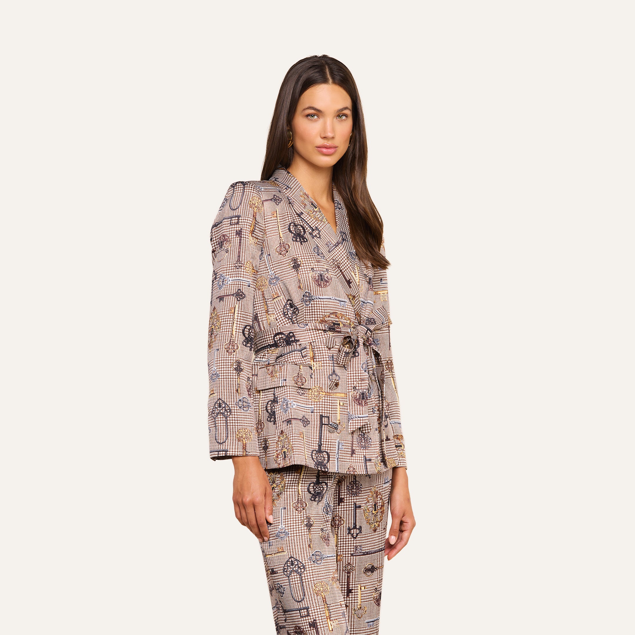 A woman stands against a plain, light background, looking at the camera while wearing a modern suiting look featuring the Aven Wrap Blazer and matching straight-leg plaid pants.