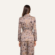 A woman stands facing away, wearing the Aven Wrap Blazer and matching wide-leg pants. The modern suiting set features a beige base with dark and light motifs, and her long brown hair is down.