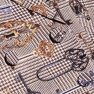 Close-up of patterned fabric from the Aven Wrap Blazer, featuring gold and black vintage keys and locks on a brown houndstooth background—perfect for modern suiting or a fashionable wrap-front blazer.