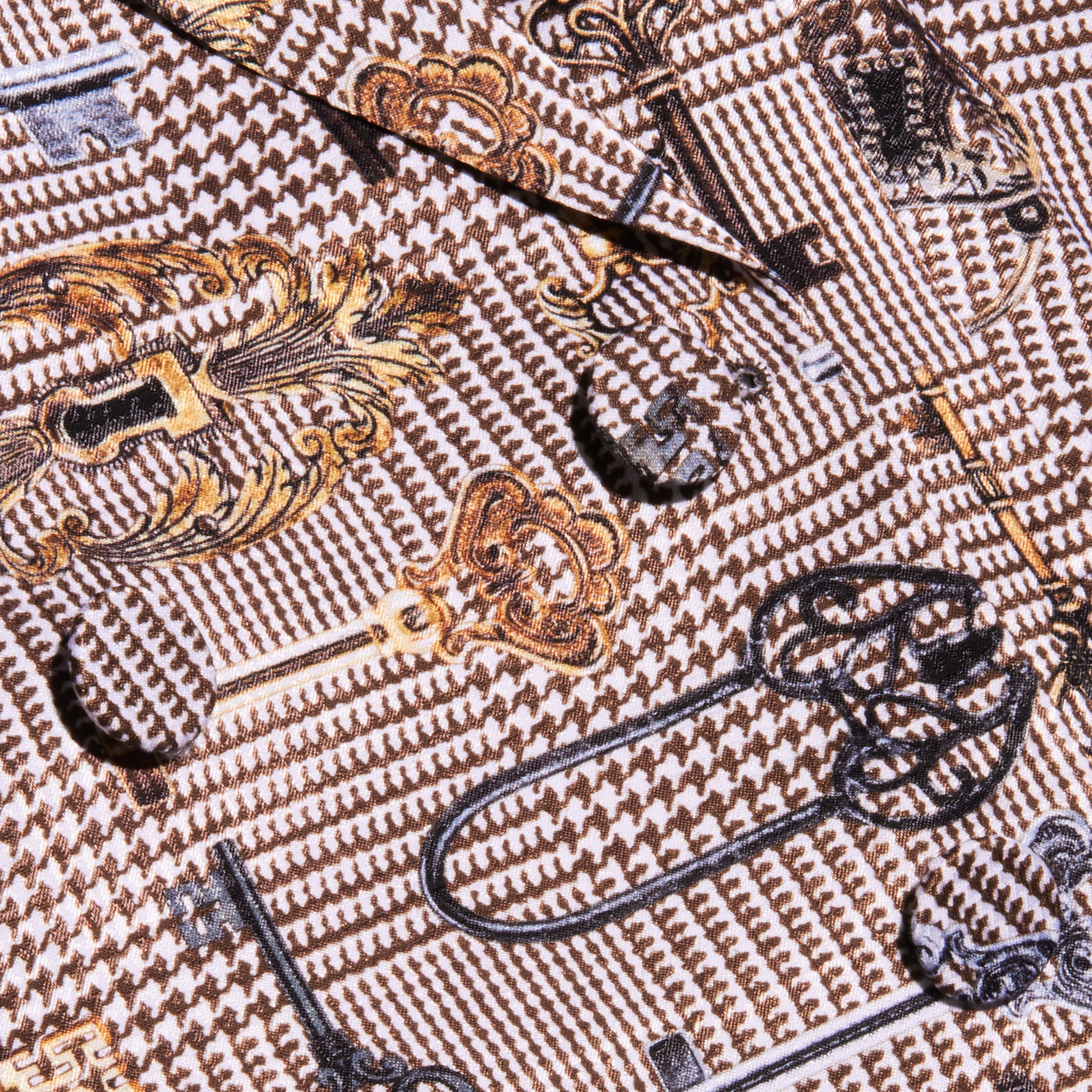 Close-up of patterned fabric from the Aven Wrap Blazer, featuring gold and black vintage keys and locks on a brown houndstooth background—perfect for modern suiting or a fashionable wrap-front blazer.