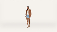 A woman walks forward wearing a brown jacket, white top, light blue shorts, and nude heels against a plain white background.