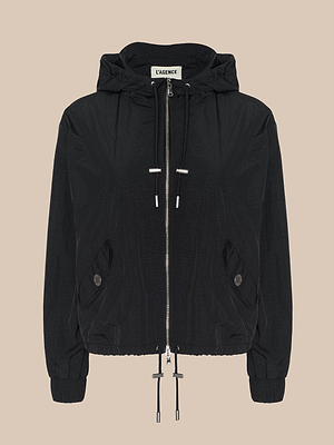 La Miro Hooded Windbreaker es una chaqueta negra repelente al agua con cremallera frontal, capucha y cordones en el dobladillo, bolsillos laterales con cierre de botón y puños elásticos, mostrada sobre un fondo beige.